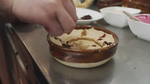 Chef prepares mediterranean starters. Adding olive oil to hummus. Plating Stock Footage 150586409