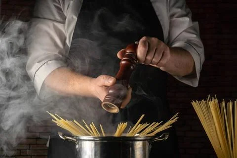 Chef prepares pasta by adding pepper from a grinder over boiling water in a.. Stock Photos