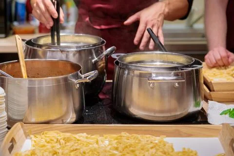 The chef prepares pasta in large metal pans. Male hands take out the pasta fr Stock Photos