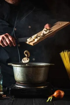 Chef prepares soup on the background of vegetables and spaghetti. Stock Photos