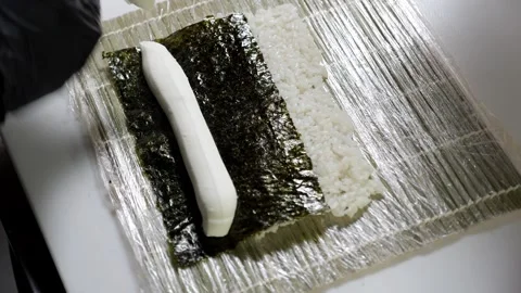 A chef prepares sushi in the kitchen, squeezing cream cheese onto the nori. Stock Footage 329275996