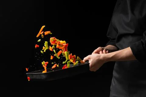 Chef prepares vegetables. freezing in motion. on black background. cooking ba Stock Photos
