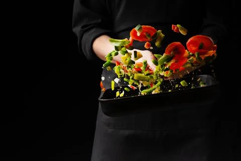 Chef prepares vegetables. freezing in motion. on black background. cooking ba Stock Photos
