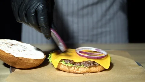 Chef preparing the burger. Close up hands of man stacking onion rings. Stock Footage 115798912