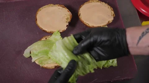 A chef preparing a burger, he puts various ingredients on a bun with sauce. Stock Footage 345132645