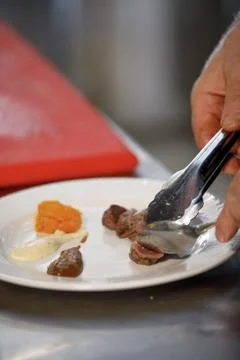 Chef is preparing a dish with meat, different sauces and pumpkin Stock Photos
