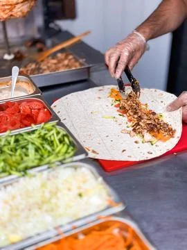 Chef preparing fresh shawarma wrap with vibrant vegetables in kitchen setting Foto stock