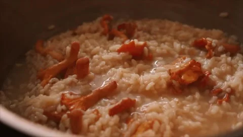 Chef preparing Italian mushroom risotto (risotto ai funghi) while adding bouillo Stock Footage 251995671