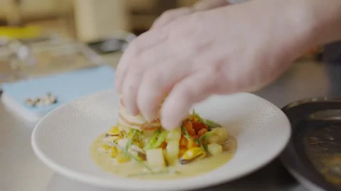 A chef is preparing a meal with a white plate of food on a table Stock Footage 306576847