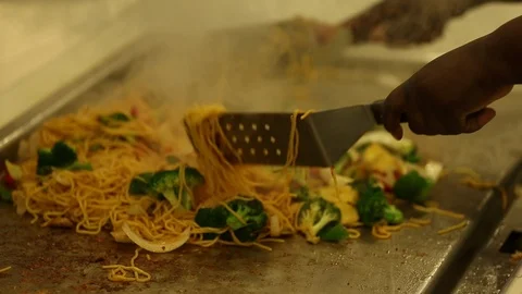 Chef preparing noodle and vegetable stir fry on large flat top hibachi gridd Stock Footage 123875544