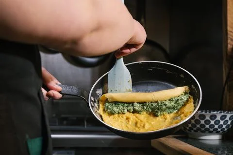 Chef preparing omelet with spinach and cheese filling Stock Photos