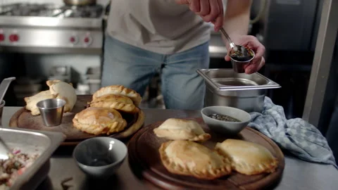 A chef preparing salsa alongside empanada in the kitchen table Video stock 238642230