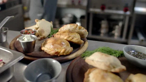 Chef preparing to serve empanada a waiter picking salsa from the kitchen table Video stock 238635739