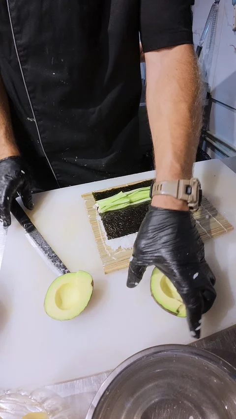 Chef preparing sushi roll with avocado and cucumber on bamboo mat, close-up of Stock Footage 314496259