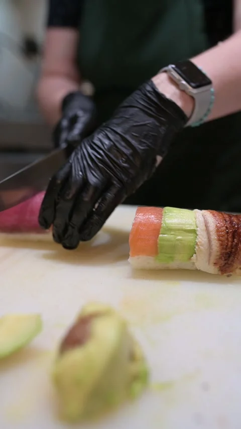 Chef preparing sushi roll with layered toppings of salmon, avocado, tuna, and Stock Footage 314500809