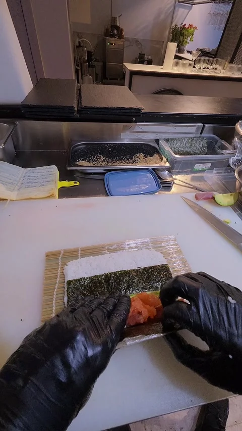 Chef preparing sushi roll with salmon and cucumber on bamboo mat in professional Stock Footage 314497692