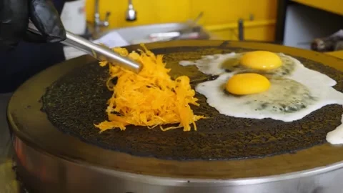 Chef preparing a unique black crepe on a professional griddle with fried eggs an Stock-Footage 345692703