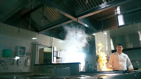 Chef a professional in the kitchen prepares a dish on the fire burning pans Stock Footage 102661038