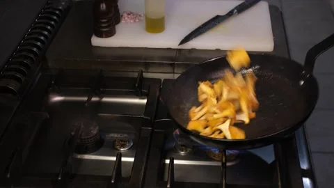Chef in professional kitchen stirring chanterelle mushrooms in pan side view clo Stock Footage 334126544