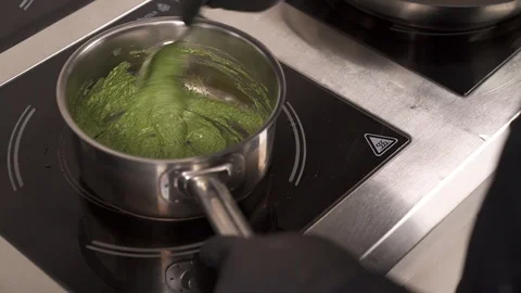 A chef in a professional kitchen whisking the spinach in a pan. Concept of Stock Footage 105494428