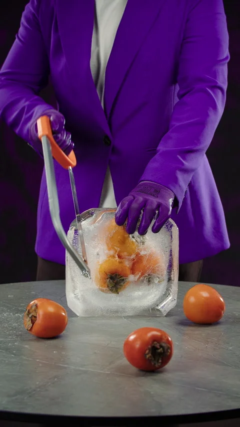 Chef in a purple jacket uses a hacksaw to saw frozen persimmons in an ice cube Stock Footage 302882358