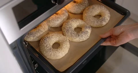 Chef pushes a baking sheet of bagels into the oven. Cooking the pastry at home Stock Footage 166576019