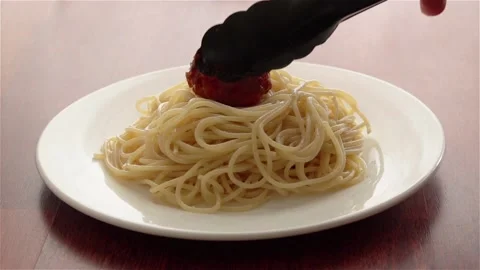 Chef put meatballs on hot spaghetti with serving tongs on white plate Vidéo 107932954