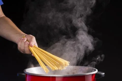 The chef put spaghetti in the pot or a pan of boiling water with hot steam or Stock Photos
