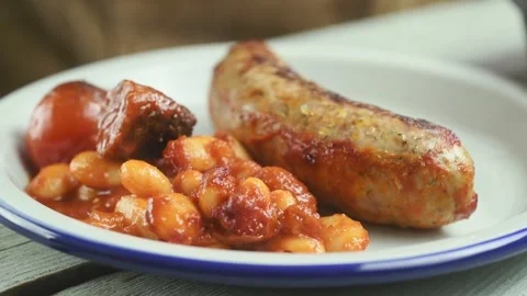 The chef puts the bean casserole in the plate with sausage. Stock Footage 202177031