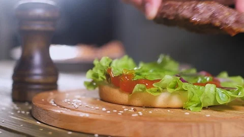 Chef puts a Burger on a bun with a leaf of salad. Top throw a slice of cheese. Video stock 111761311