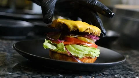 The chef puts a cutlet with cheese in a hamburger in black gloves slow motion Stock Footage 230076128