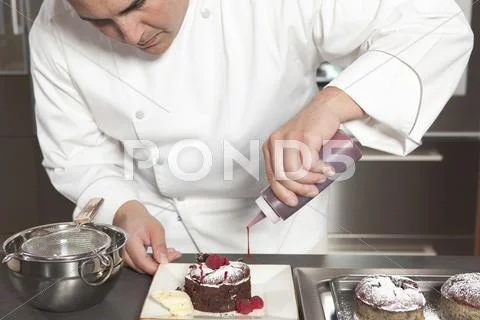 Chef Puts Finishing Touches On Chocolate Cake At Kitchen Counter Stock Photos