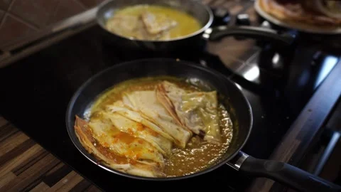 Chef puts the folded pancakes into the boiling orange sauce in the pans Stock-Footage 267922916