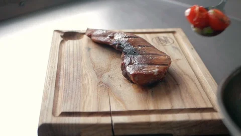 Chef puts fried tomatoes with onions on a piece of baked meat on a wooden board Stock Footage 92938152
