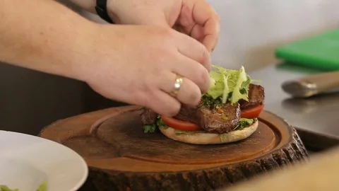 Chef puts green lettuce leaf on a burger meat Video stock 74716070