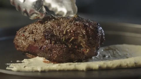 The chef puts a juicy, seared steak on a plate with sauce. Video stock 239007480