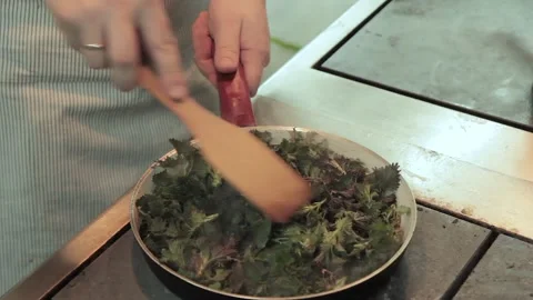 The chef puts the leaves of the nettle into the pan in restaurant kitchen. Chef Stock Footage 131335951