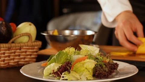 Chef puts mango sliced into thin slices on a plate of green salad leaves Stock Footage 116683552