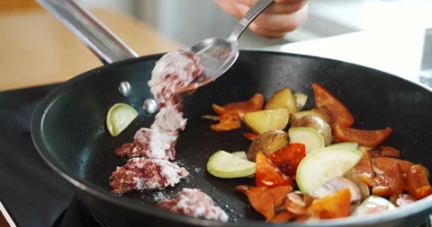 Chef puts meat into pan with frying vegetables, cooking them together with oil. Stock Footage 133392554