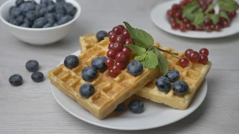 The chef puts a mint leaf on a plate of maple syrup-poured waffles garnished Stock Footage 172568978