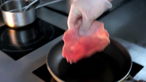 Chef puts piece of raw meat on a hot frying pan with oil. Stock Footage 132427512