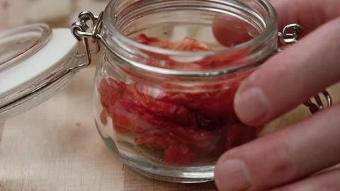 Chef puts pieces sun dried tomatoes with garlic and seasonings in glass jar. Stock Footage 253760548