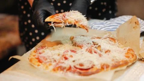 The chef puts pizza on plates in black latex gloves. Cooking during the Stock Footage 132031889