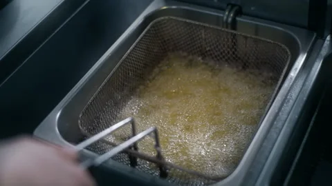 Chef puts raw potatoe to the boiling oil for making fries in slow motion Stock Footage 143779293