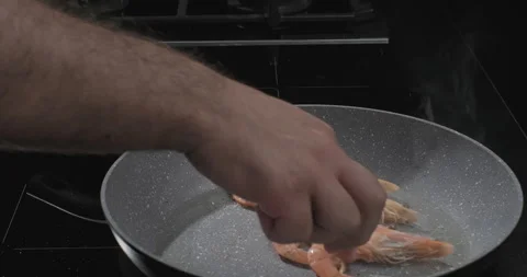 Chef puts shrimp in a frying pan on black background. Cooking seafood. Slow Stock Footage 249984136