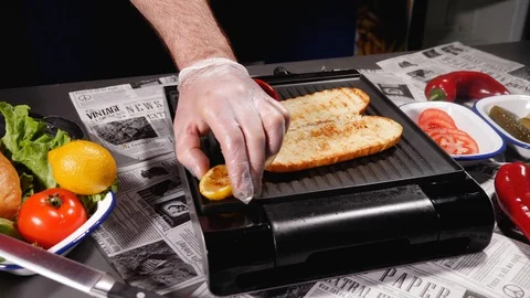 The chef puts a slice of lemon on a hot grill plate, where bread is toasted Stock Footage 128291086