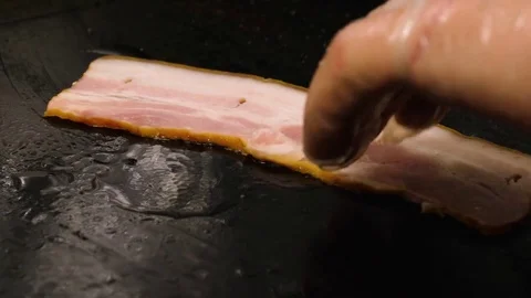 Chef puts slice of raw bacon on the frying surface with oil, 4K 60 FPS Stock Footage 76952385