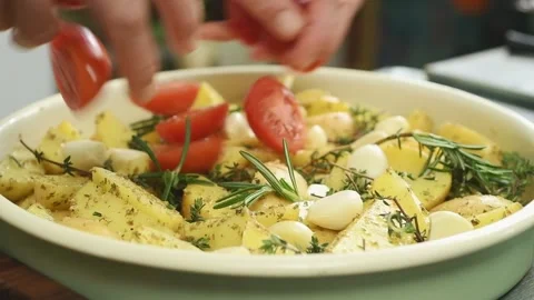 The chef puts sliced cherry tomatoes in the tray with flavored potatoes. Stock Footage 207022026
