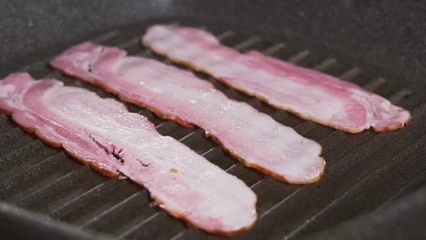 Chef puts slices of fresh raw bacon on the frying pan surface with oil. 스톡 동영상 334642357