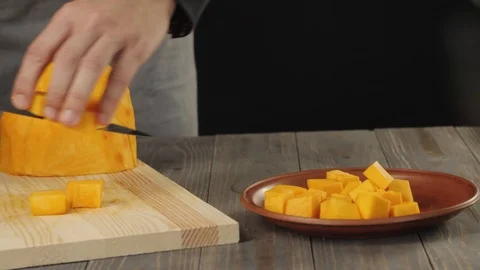 Chef puts slices of pumpkin in a brown plate on a wooden table. Side view. 4K Stock Footage 126419321
